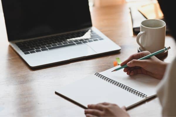 Person writing in notebook with laptop